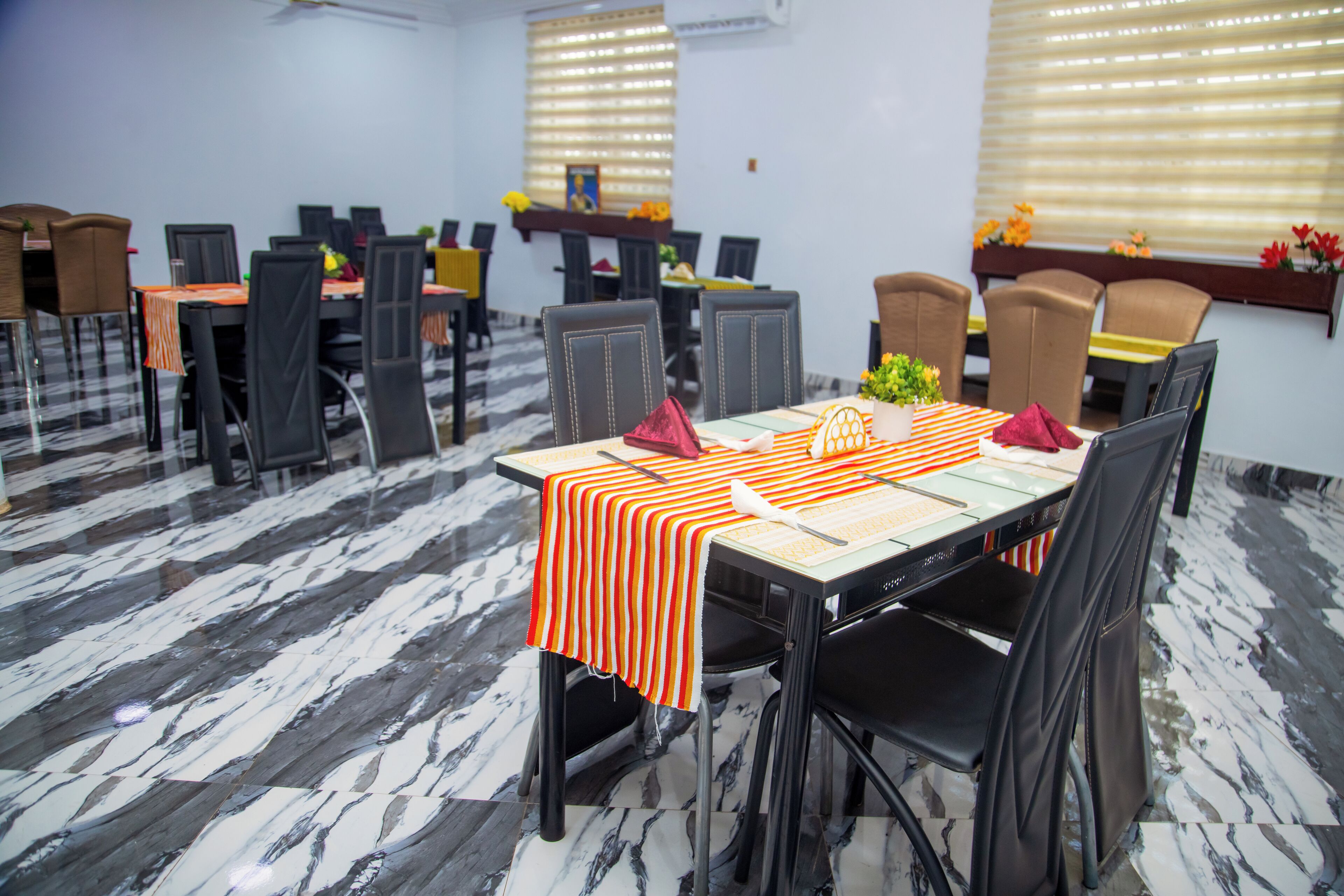 A conference room with a marble floor, tables with orange-striped tablecloths, and black chairs.