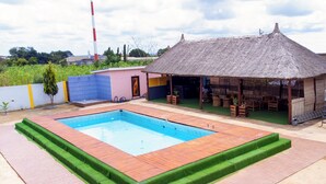 Piscina con cubierta de madera y bordes de césped artificial verde.