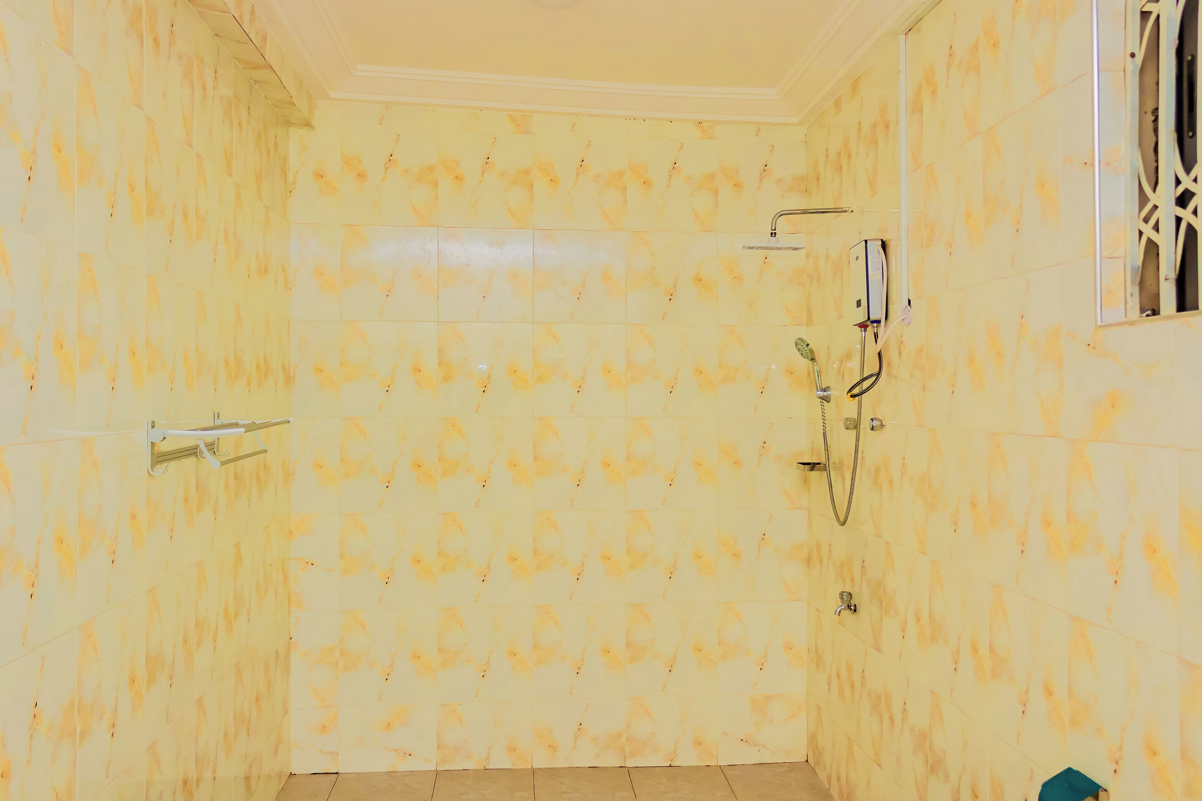 A bathroom with yellow patterned tiles, a shower, and a window with a metal grille.