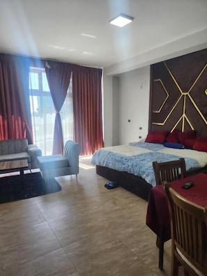 A modern hotel room with a large bed, a sofa, a dining table, and a chair. - Rendez-vous Hotel (Addis Ababa)