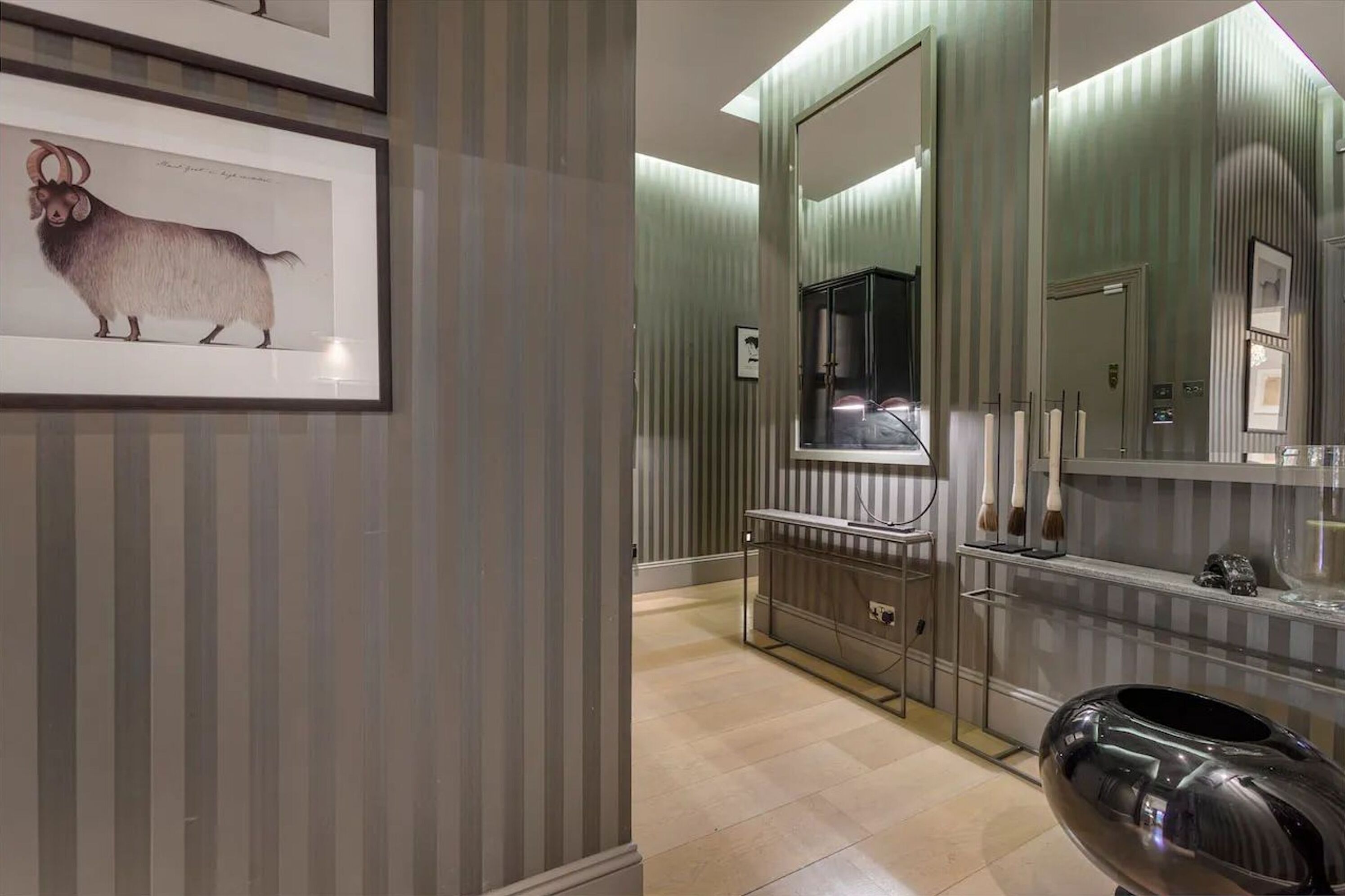 A modern bathroom with striped wallpaper, a framed animal illustration, a vanity with a mirror, and a large bathtub.