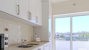 A modern kitchen with a built-in oven, microwave, and washing machine, a sink, and a view of the city through large windows. - #320 Family Apartment in the City Center (Albufeira)