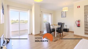 A modern apartment with a dining area, a large sliding glass door leading to a balcony, and a fire extinguisher mounted on the wall. - #320 Family Apartment in the City Center (Albufeira)