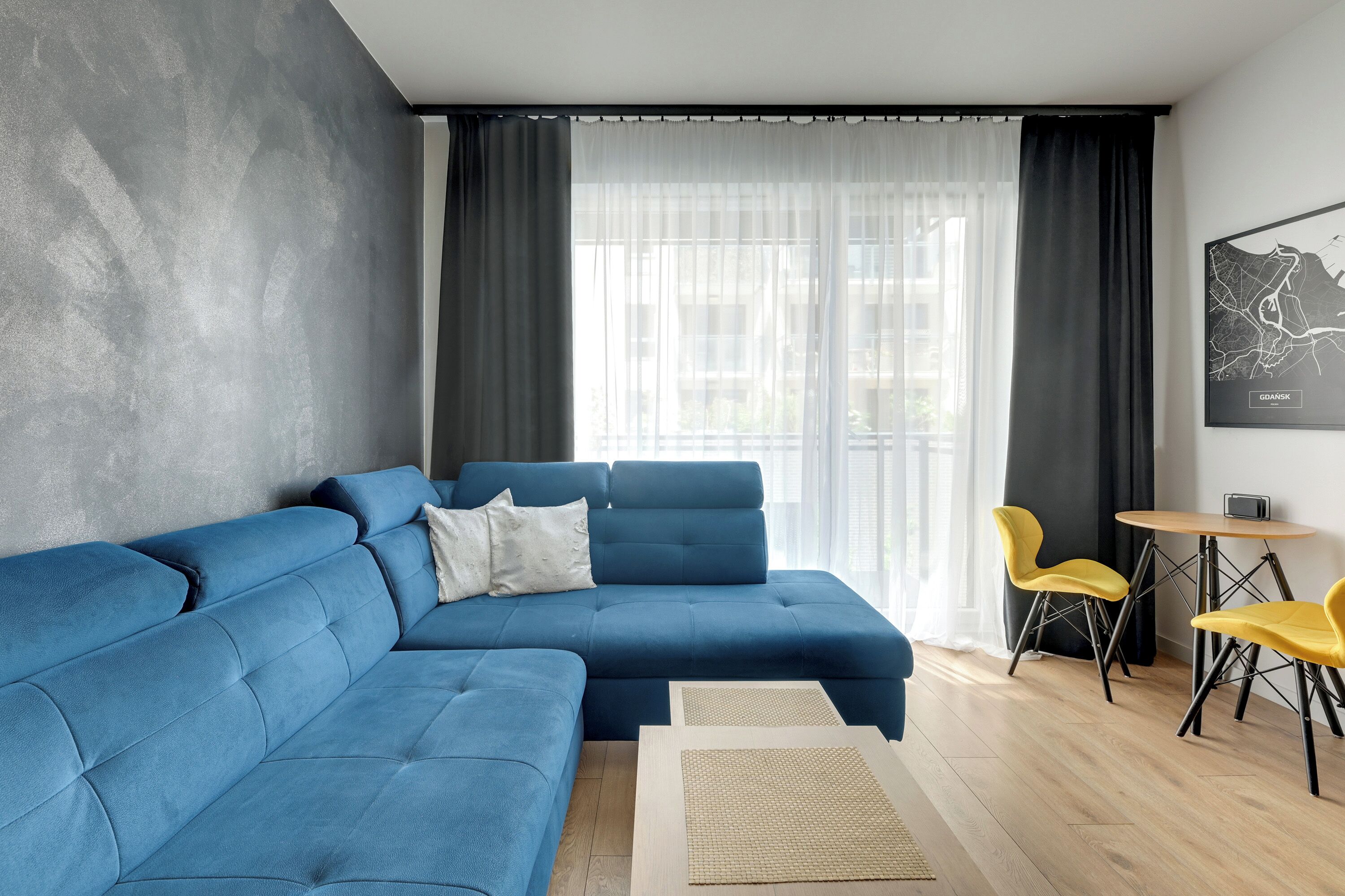A modern living room with a blue sectional sofa, two yellow chairs, a small round table, and a map on the wall.