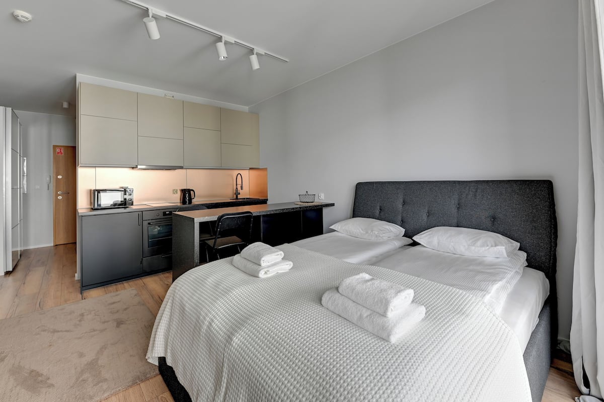 A modern hotel room with a large bed, a desk, and a kitchenette.