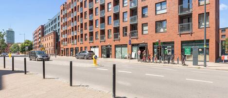 Um edifício com várias andares, fachada de tijolo, diversas varandas e entrada no nível do solo com área de estacionamento para bicicletas.