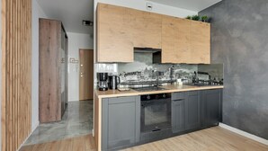 A modern kitchen with wooden cabinets, a built-in oven, and a backsplash with a cityscape design. - RentPlanet - Studio Wałowa (Gdańsk)