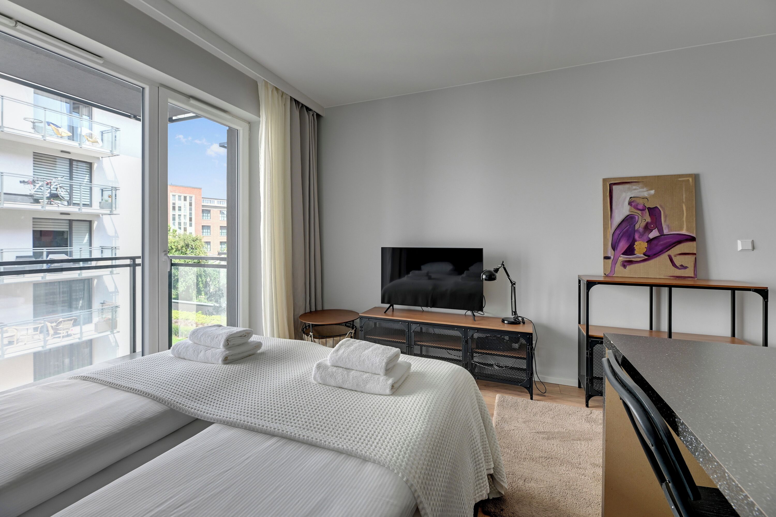 Quarto de hotel com uma cama grande, televisão, escrivaninha e um quadro na parede.