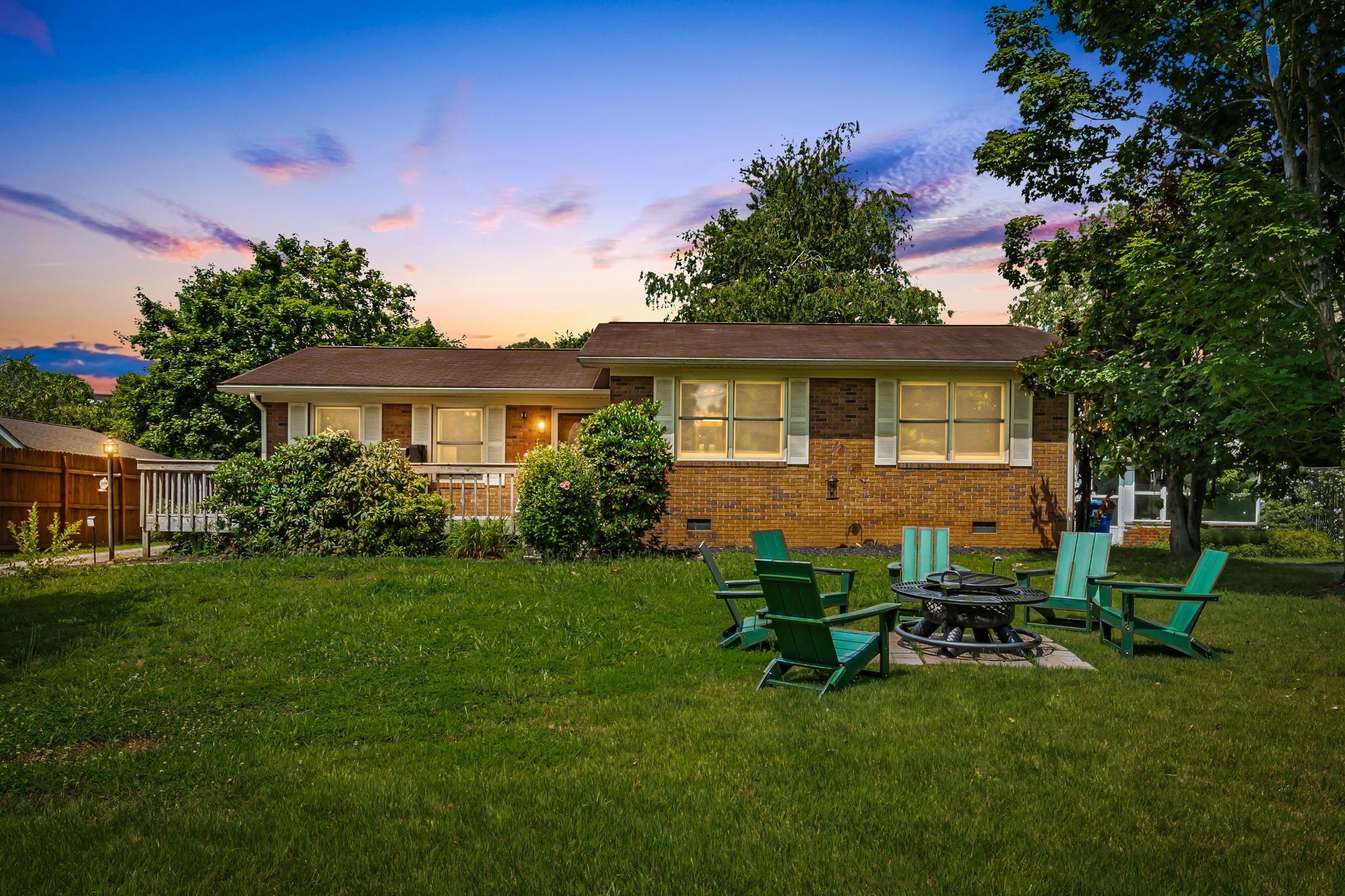 A two-story house with a brick exterior, a front porch, and a backyard with green chairs and a fire pit.