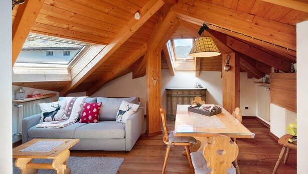 A cozy attic room with a loft bed, a dining table with chairs, a sofa with decorative pillows, and a skylight.