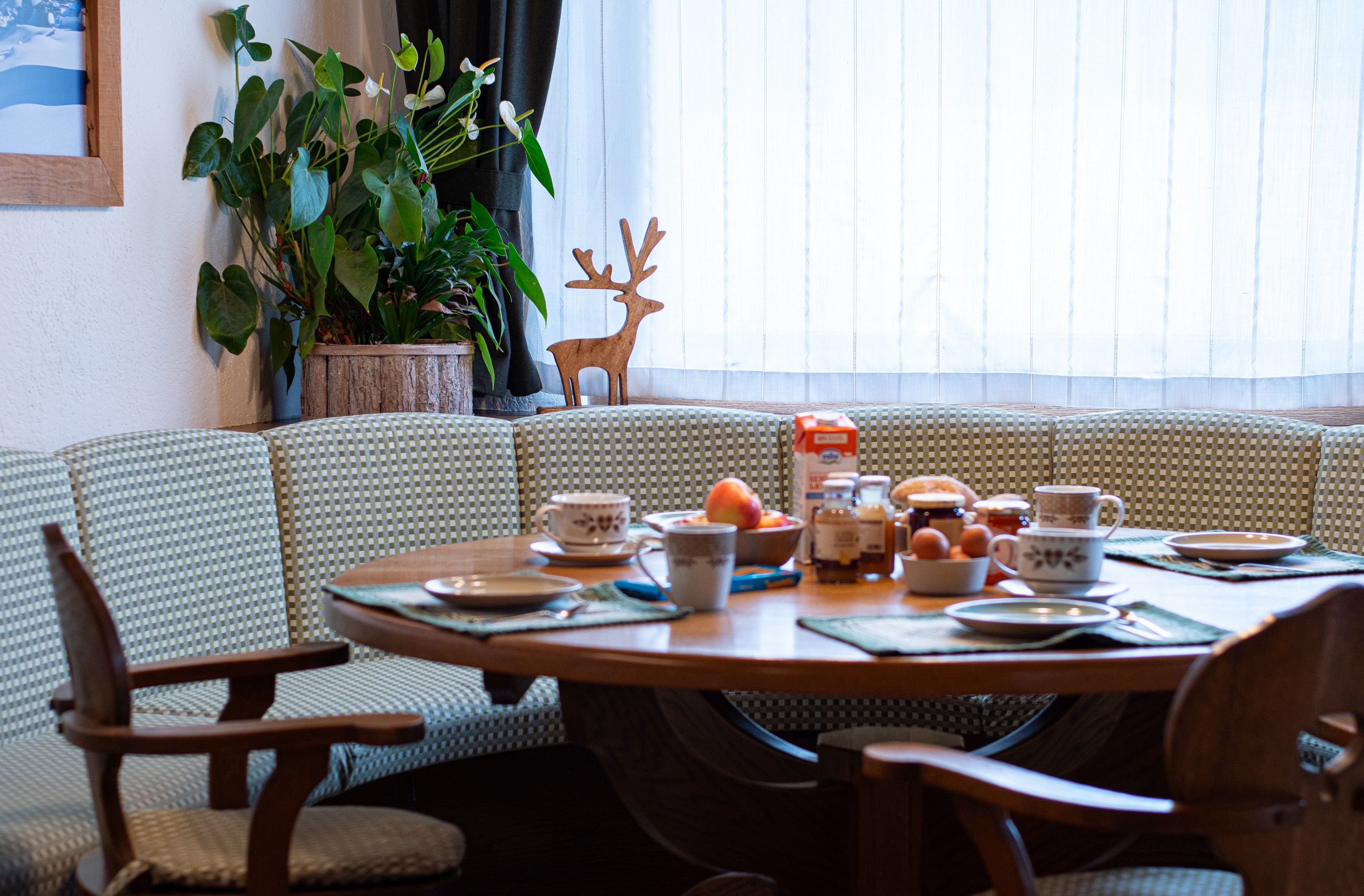 Un área de comedor con un sofá a cuadros, sillas de madera, una mesa dispuesta con platos, tazas y un frutero.