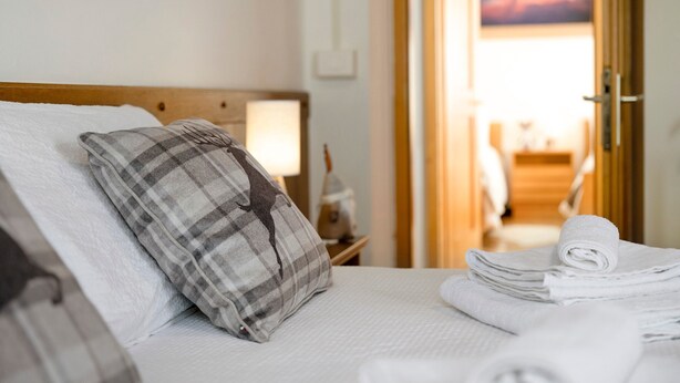 A neatly made bed with a plaid pillow, a stack of white towels, and a wooden headboard. - Apartment 'Il Feudo' with Mountain View, Balcony and Wi-Fi (Predazzo)