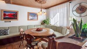 A cozy room with a round wooden table, a green sofa, and a large wall clock. - Apartment 'Il Feudo' with Mountain View, Balcony and Wi-Fi (Predazzo)