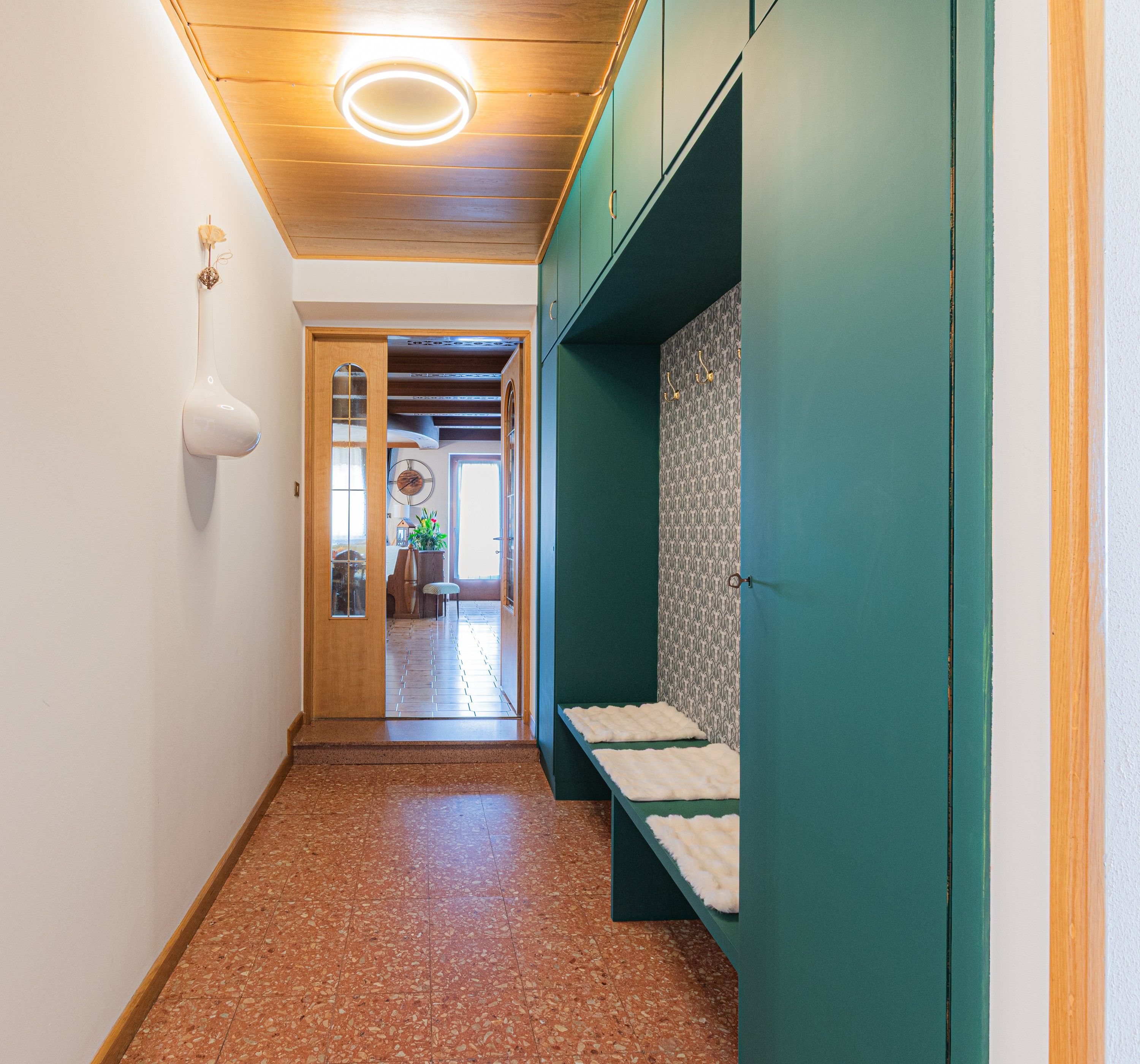 Ein Flur mit Holzboden, einer Tür zu einem anderen Raum und einer Wand in Grün mit einem gemusterten Design.
