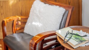 A wooden chair with a white fluffy pillow, a book, and a pair of glasses on a round wooden table. - Apartment 'Il Feudo' with Mountain View, Balcony and Wi-Fi (Predazzo)