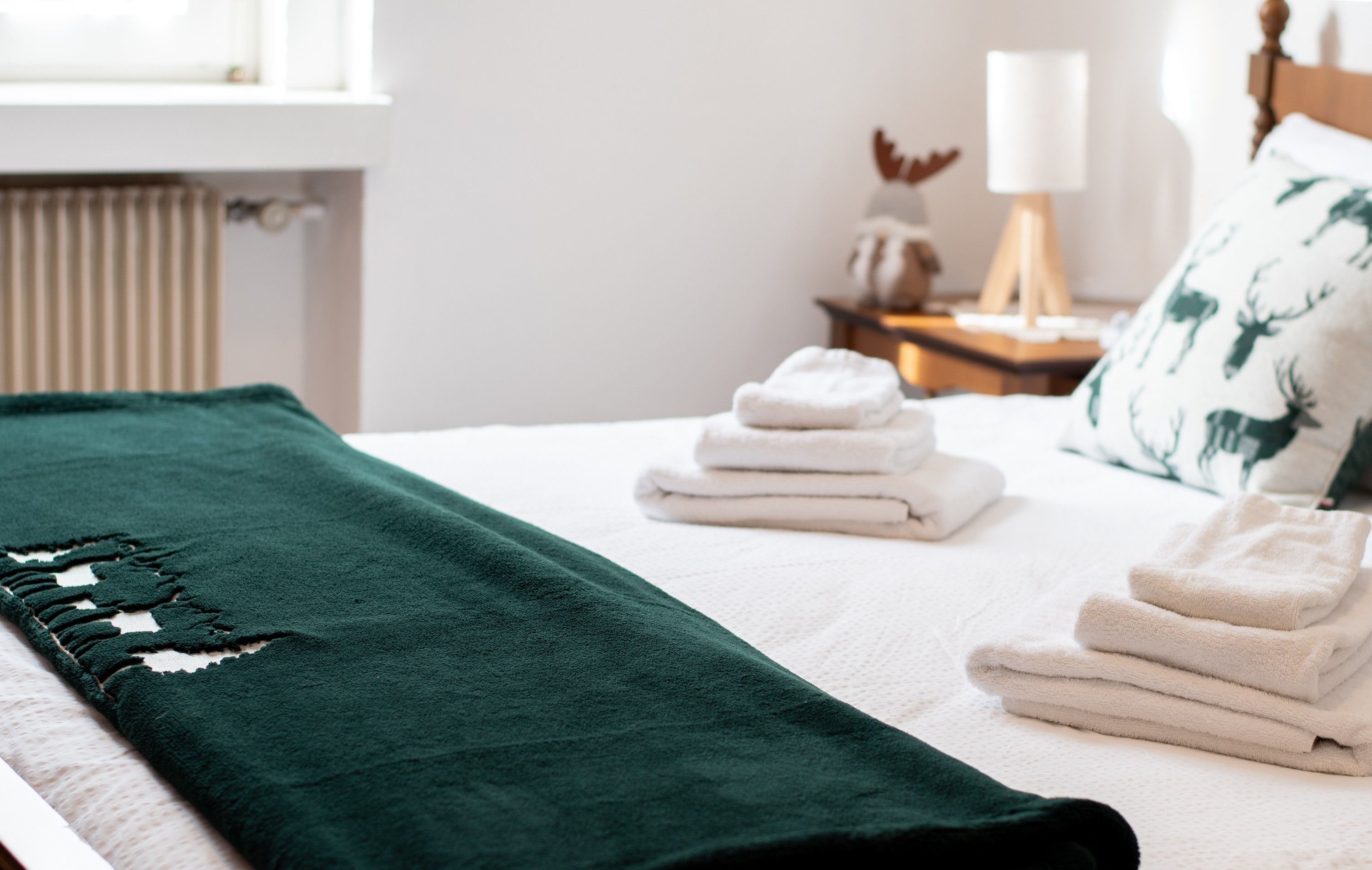 A neatly made bed with a green blanket, white linens, and a stack of folded towels.