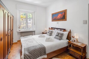 Une chambre avec un lit en bois, une fenêtre donnant sur un beau paysage, un radiateur et une armoire en bois.
