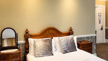 Una cama bien hecha con almohadas, una mesita de noche de madera con un espejo y un aparador con cajones.