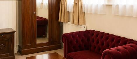 Una habitación con una mesa de madera, un sofá rojo, un armario de madera y una ventana con cortinas.