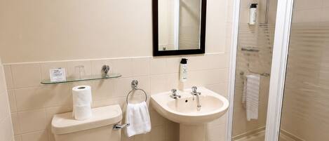 A bathroom with a toilet, sink, mirror, and glass shower enclosure.