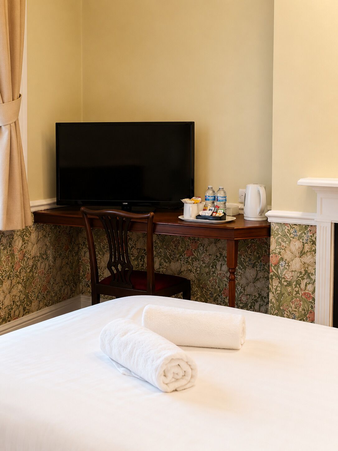 Habitación de hotel con cama, escritorio con televisor, silla, cafetera y bandeja con artículos de aseo.