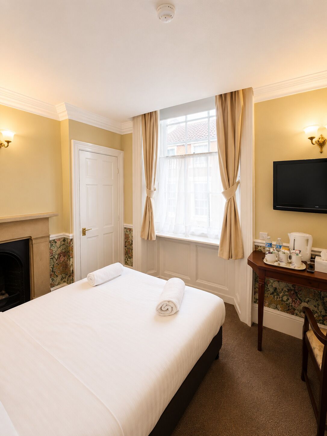 A hotel room with a bed, a desk with a coffee maker, a television, a fireplace, and curtains.