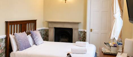 A hotel room with a bed, a chair, a desk with a lamp, a fireplace, and a television.