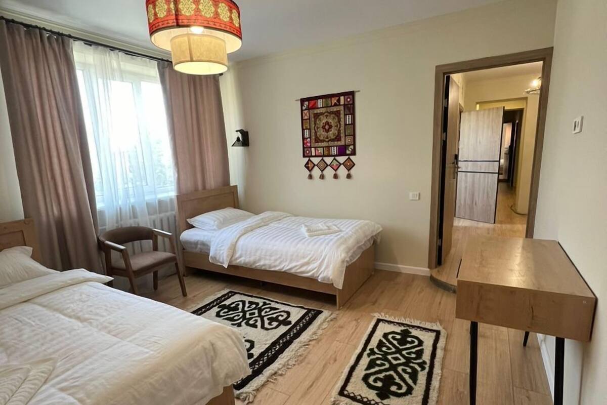 Ett hotellrum med två sängar, ett skrivbord, en stol, en hängande lampa och en väggbonad.
