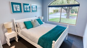 A bedroom with a white bed, teal pillows, a teal throw blanket, a bedside lamp, and framed artwork on the wall. - Aqua Tides – Stylish Waterfront Escape in Busselton (Geographe)