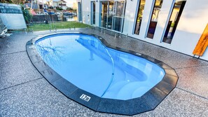 A swimming pool with a 2m depth marker, surrounded by a paved area and a modern building with large windows. - Aqua Tides – Stylish Waterfront Escape in Busselton (Geographe)