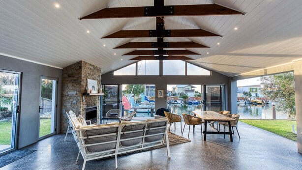 A spacious living area with a stone fireplace, comfortable seating, and a view of a marina through large windows. - Aqua Tides – Stylish Waterfront Escape in Busselton (Geographe)