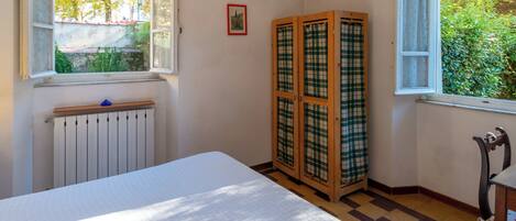 A room with a bed, a radiator, a window with a view of trees, and a checkered cabinet.