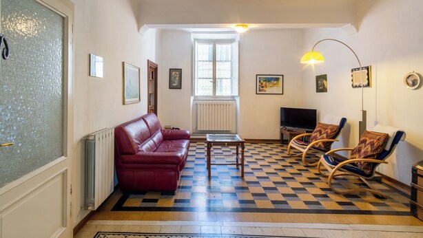 A living room with a red sofa, a coffee table, and patterned chairs. There is a radiator, a TV, and framed pictures on the wall. - The key to time (Lucca)