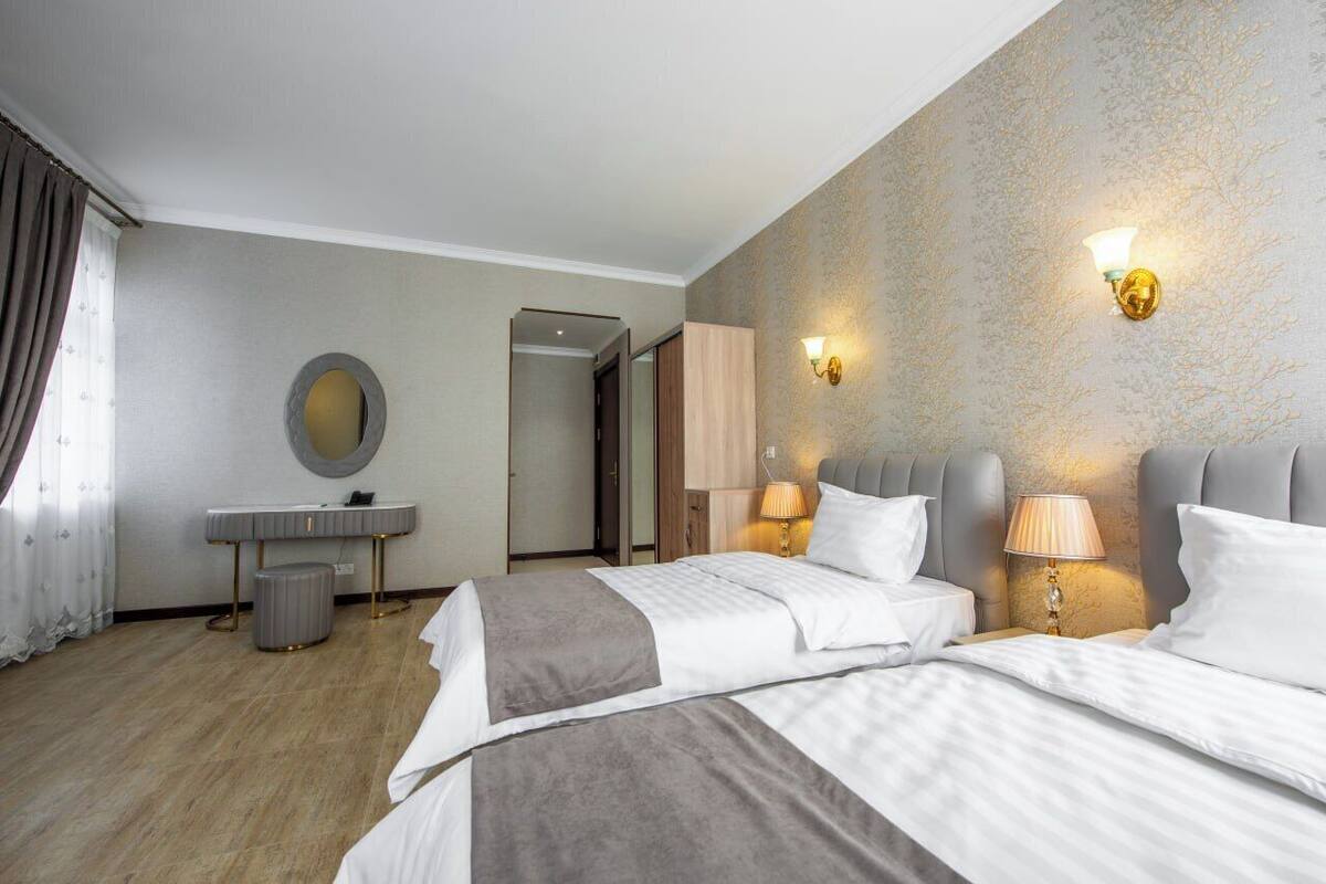 A hotel room with two beds, a vanity with a mirror, a desk, and a door leading to another room.