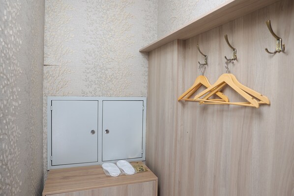A small, private room with a wooden bench, a pair of slippers, and a coat rack with hangers. -  Eco Boutique Emerald Hotel (Tashkent)