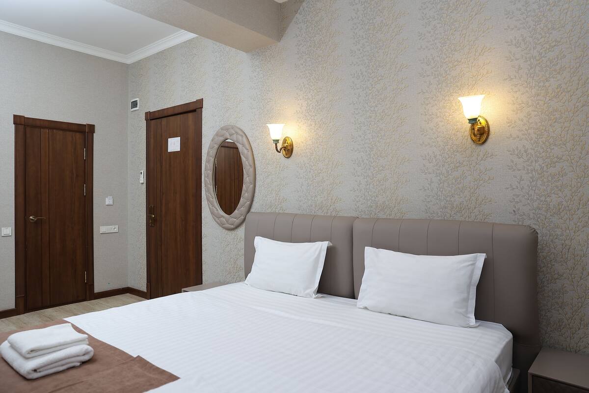 A hotel room with a large bed, two wall-mounted lights, a wooden door, and a round mirror.