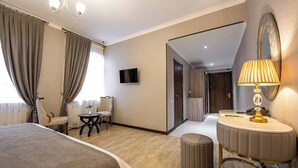 Quarto de hotel com cama, escrivaninha, cadeira, televisão, abajur e espelho.