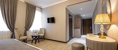 A hotel room with a bed, a desk, a chair, a TV, a lamp, and a mirror.