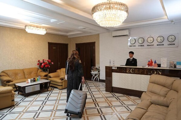 A reception area with a reception desk, a chandelier, clocks displaying times from various cities, and a patterned floor. -  Eco Boutique Emerald Hotel (Tashkent)