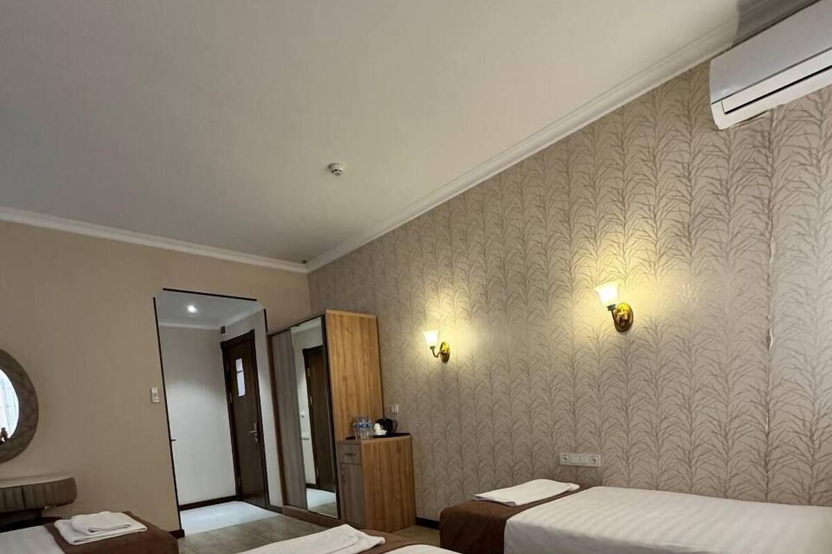 A hotel room with two beds, a mirror, a wardrobe, and a wall-mounted air conditioner.