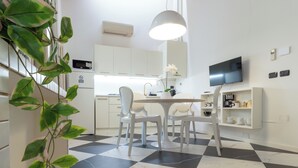 A modern kitchen with white cabinetry, a checkered floor, a dining table with chairs, a pendant light, and a TV mounted on the wall. - Designer loft in a central location with Jacuzzi in the bedroom (Rimini)