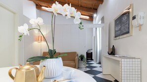 A room with a white table, a gold teapot, a white cup, and a white vase with orchids. There is a brown sofa, a small table with a lamp, and a checkered floor. - Designer loft in a central location with Jacuzzi in the bedroom (Rimini)