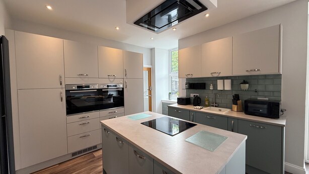 A modern kitchen with built-in appliances, a central island, and a window providing natural light.