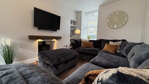A modern living room with a flat-screen TV, a fireplace, a sofa set, and a clock on the wall.