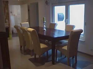 A dining area with a rectangular table and six chairs, a door with a window, and a wall-mounted clock.