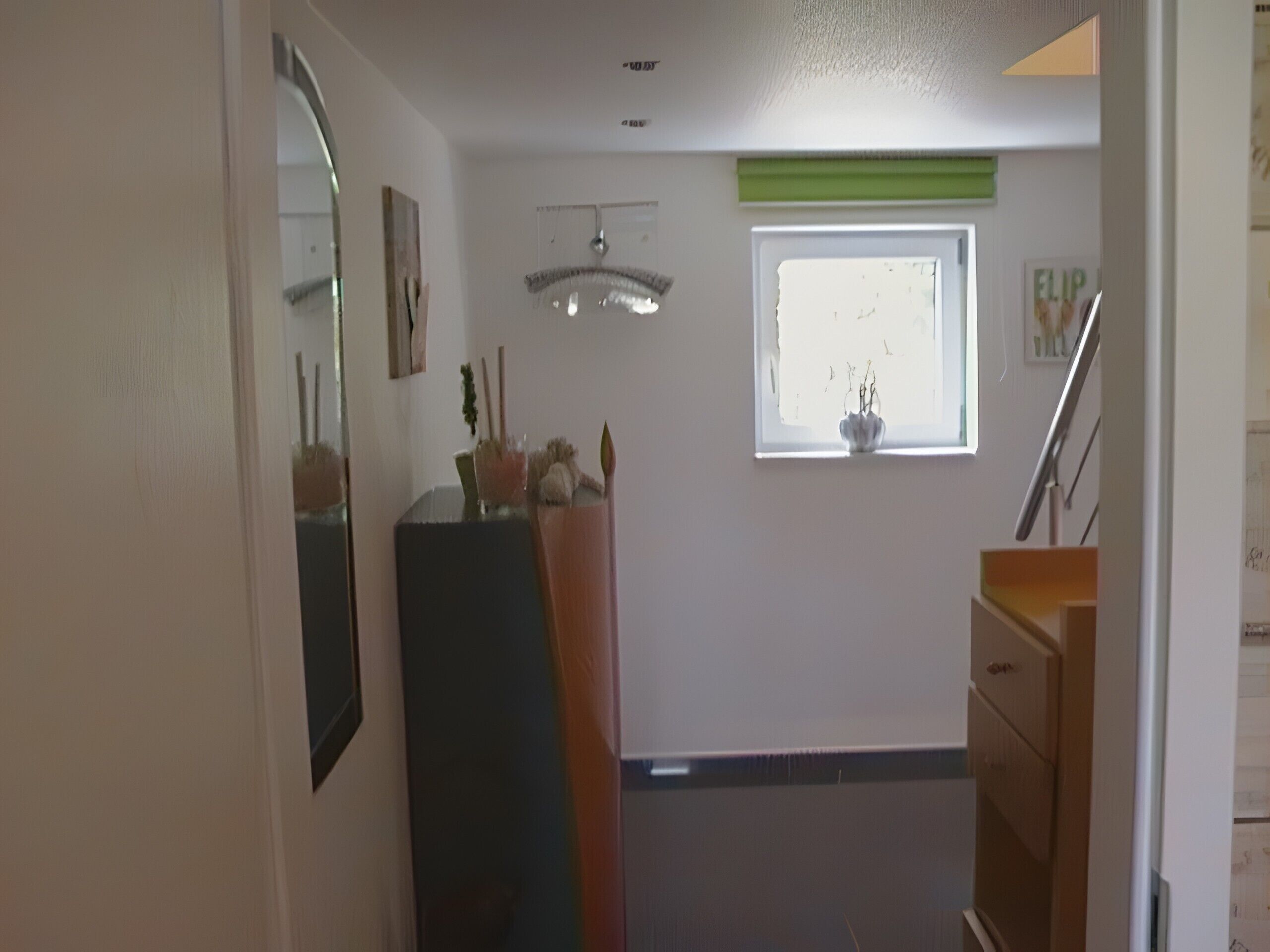 A hallway with a mirror, a small window with a plant, a ceiling fan, and a staircase.