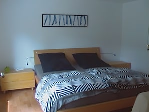 A bedroom with a bed, two pillows, a nightstand, a lamp, and a wall art piece.