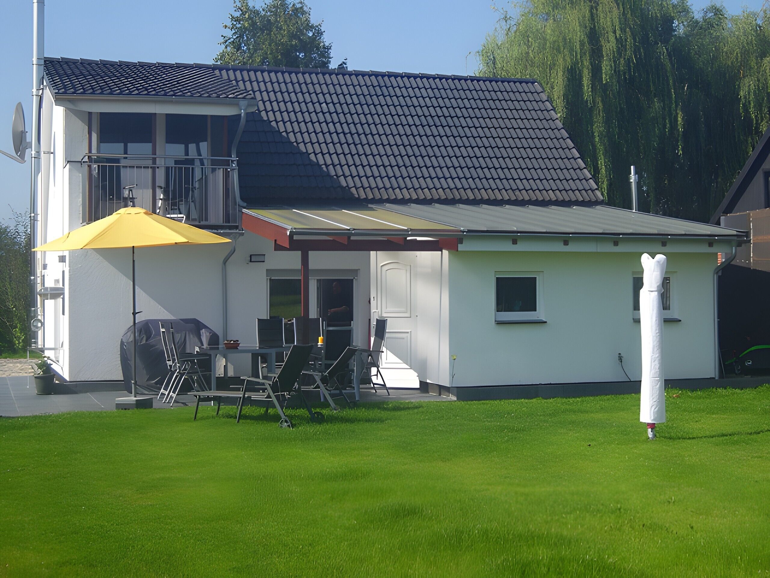 Een tweelaags huis met een terras, tuinmeubels en een overdekte zithoek.