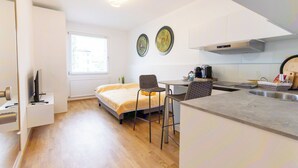 Habitación de hotel compacta con cama, una pequeña mesa de comedor, kitchenette y ventana.