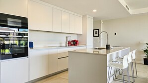 A modern kitchen with white cabinets, a built-in oven, and a central island with bar stools. - Townhouse with sea views Evergreen Homes (Mijas Costa)